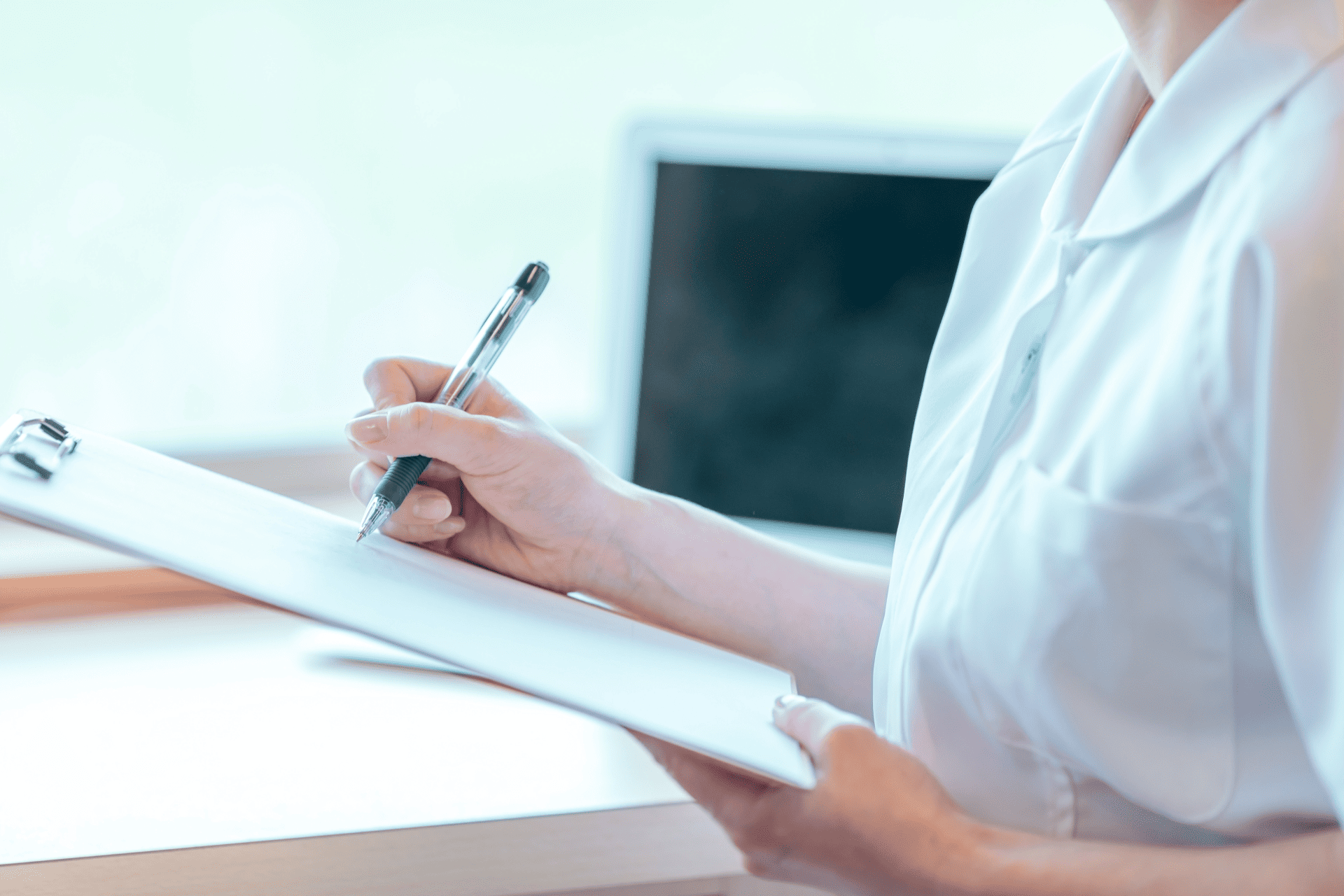 ペンとクリップボードを持ってメモを取る医療従事者