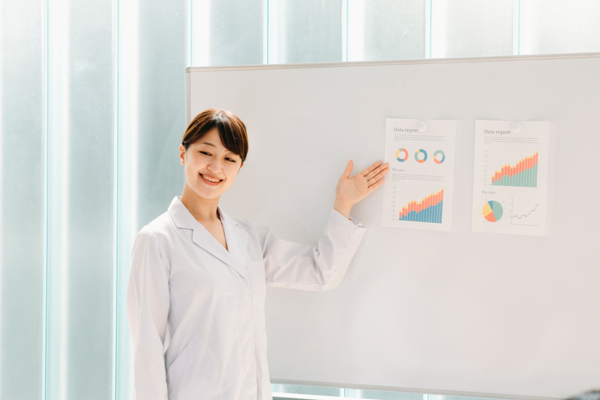 会議でホワイトボードに貼ってある資料を指して、説明をする女性医師