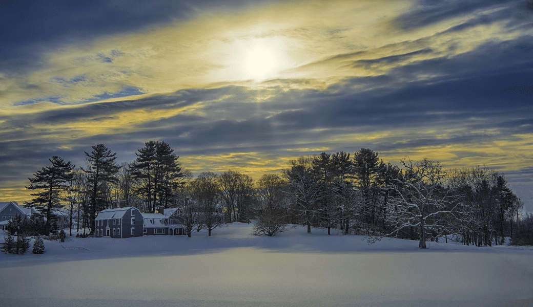 雪景色の中に佇む家々。冬の夕陽が雲間から差し込む、穏やかな風景。
